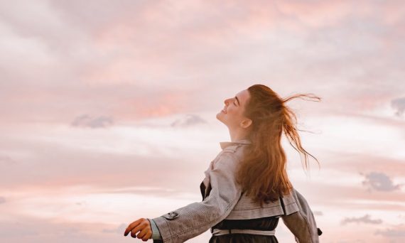 A woman joyfully embraces the sunset with arms spread in freedom, capturing serenity in nature.